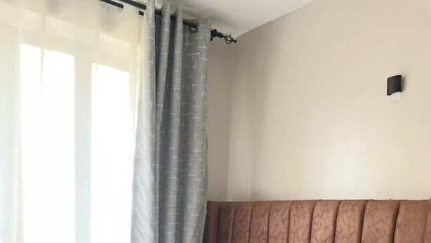Cama bem arrumada com lençóis brancos, cabeceira marrom e dois travesseiros em azul e amarelo.