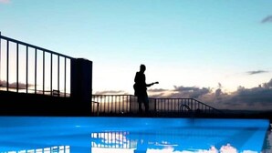 Uma pessoa ao lado de uma piscina com guarda-corpo, sob um céu claro.
