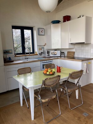 Une cuisine avec des meubles blancs, une fenêtre, un évier, un four à micro-ondes, une cuisinière et une table à manger avec des chaises.