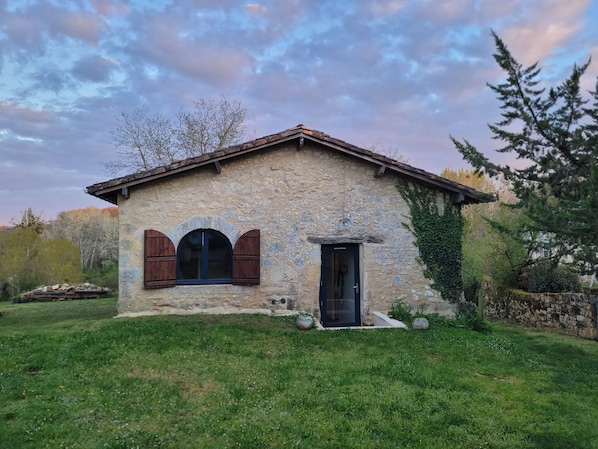 Un bâtiment en pierre avec un toit en pente, une petite entrée et une fenêtre avec des volets.
