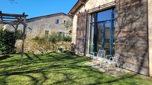 Un bâtiment en pierre doté d’une pergola en bois, d’une cour verdoyante et d’une terrasse avec des chaises en métal.