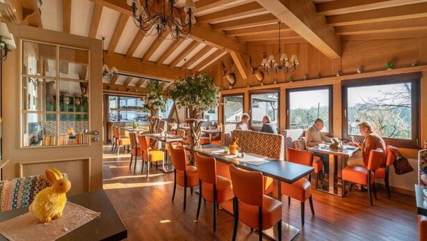 Un restaurante con vigas de madera, sillas naranjas y mesas.