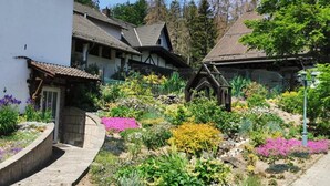 Un pueblo europeo tradicional con casas de piedra, un puente de madera y un jardín bien cuidado con diversas plantas y flores.