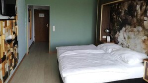 Una habitación de hotel con una cama, un televisor montado en la pared y un adorno de madera en la pared.