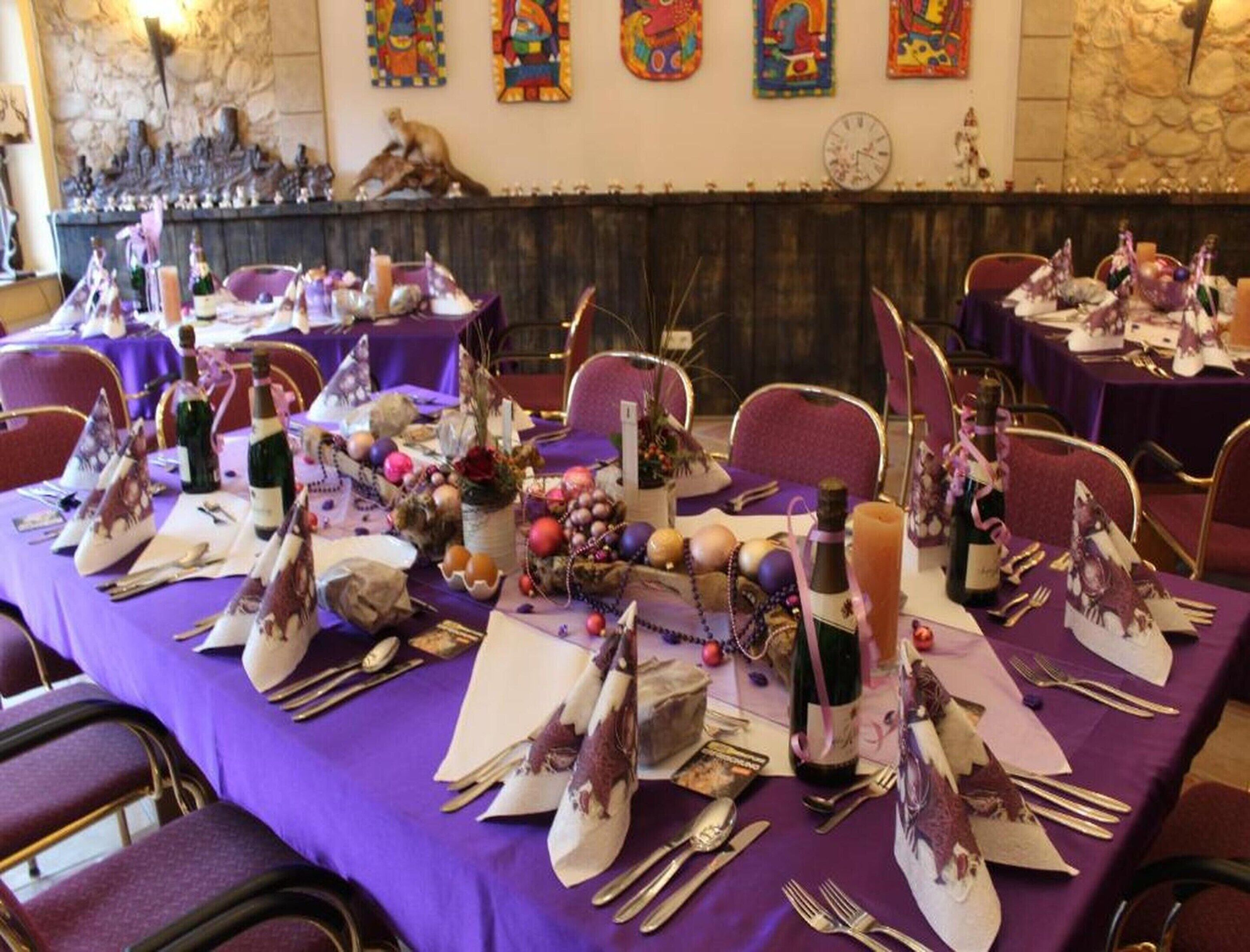 Un salón de banquetes con mesas dispuestas para un evento formal, con manteles morados, cubertería y centros de mesa decorativos.