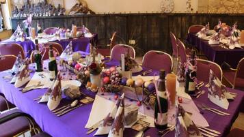 Un salón de banquetes con mesas dispuestas para un evento formal, con manteles morados, cubertería y centros de mesa decorativos.
