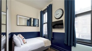 A single bed with a white mattress and pillows, a wall clock, a mirror, and a window with blue curtains. - En-Suite City View Room Near Brick Lane Shoreditch - Near Tower Bridge, London (London)