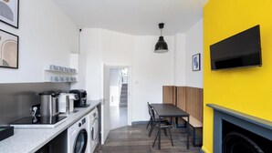 A modern kitchen with a washing machine, a dining area with a bench, and a TV mounted on a yellow wall. - En-Suite City View Room Near Brick Lane Shoreditch - Near Tower Bridge, London (London)