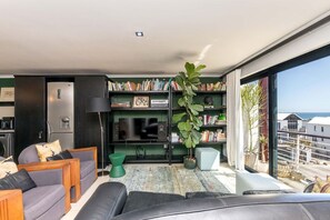 Ein modernes Wohnzimmer mit einer großen Bücherwand, einem Flachbildfernseher und Meerblick durch große Fenster.