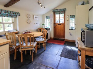 A cozy kitchen with a wooden table, chairs, a refrigerator, and a door with a window. - Beckside Studio (Penrith)
