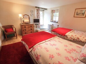 A bedroom with two beds, a dresser, a chair, a television, and a window with curtains. - Beckside Studio (Penrith)