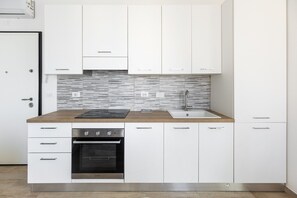 A modern kitchen with white cabinets, a stainless steel oven, a black induction cooktop, and a tiled backsplash. - Menganti White Apartment by Wonderful Italy (Bologna)
