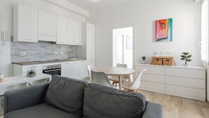Una cocina moderna con armarios blancos, un sofá gris, una mesa de comedor con sillas y un cuadro colorido en la pared.