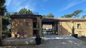 Un bâtiment en pierre avec une enseigne indiquant « ACCUEIL » et un espace extérieur abrité avec des tables et des chaises.