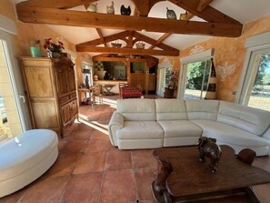 Ein geräumiger Wohnbereich mit einem großen, weißen Sofa, Holzmöbeln und einem Fliesenboden.