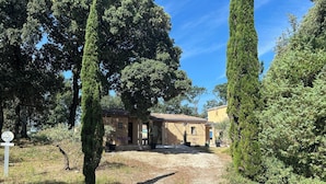 Un bâtiment rustique avec un toit en tuiles, entouré de grands arbres et accessible par un chemin de gravier.