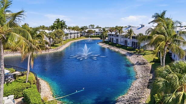 Um resort com um elemento central de água, palmeiras e uma fileira de edifícios brancos.