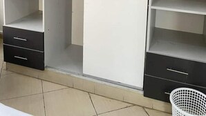 A wardrobe with multiple shelves and drawers, a hanging iron, and a laundry basket. - Snowhaven Kitengela| Modern, Secure Stay near Town (Kitengela)