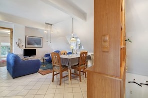 Ein Wohnzimmer mit einem blauen Sofa, einem Esstisch mit Stühlen, einem Fernseher und einem Bild an der Wand.