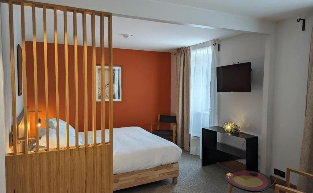 A hotel room with a bed, a desk, a TV, and a window with curtains.