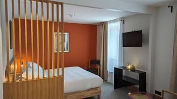A hotel room with a bed, a desk, a TV, and a window with curtains.