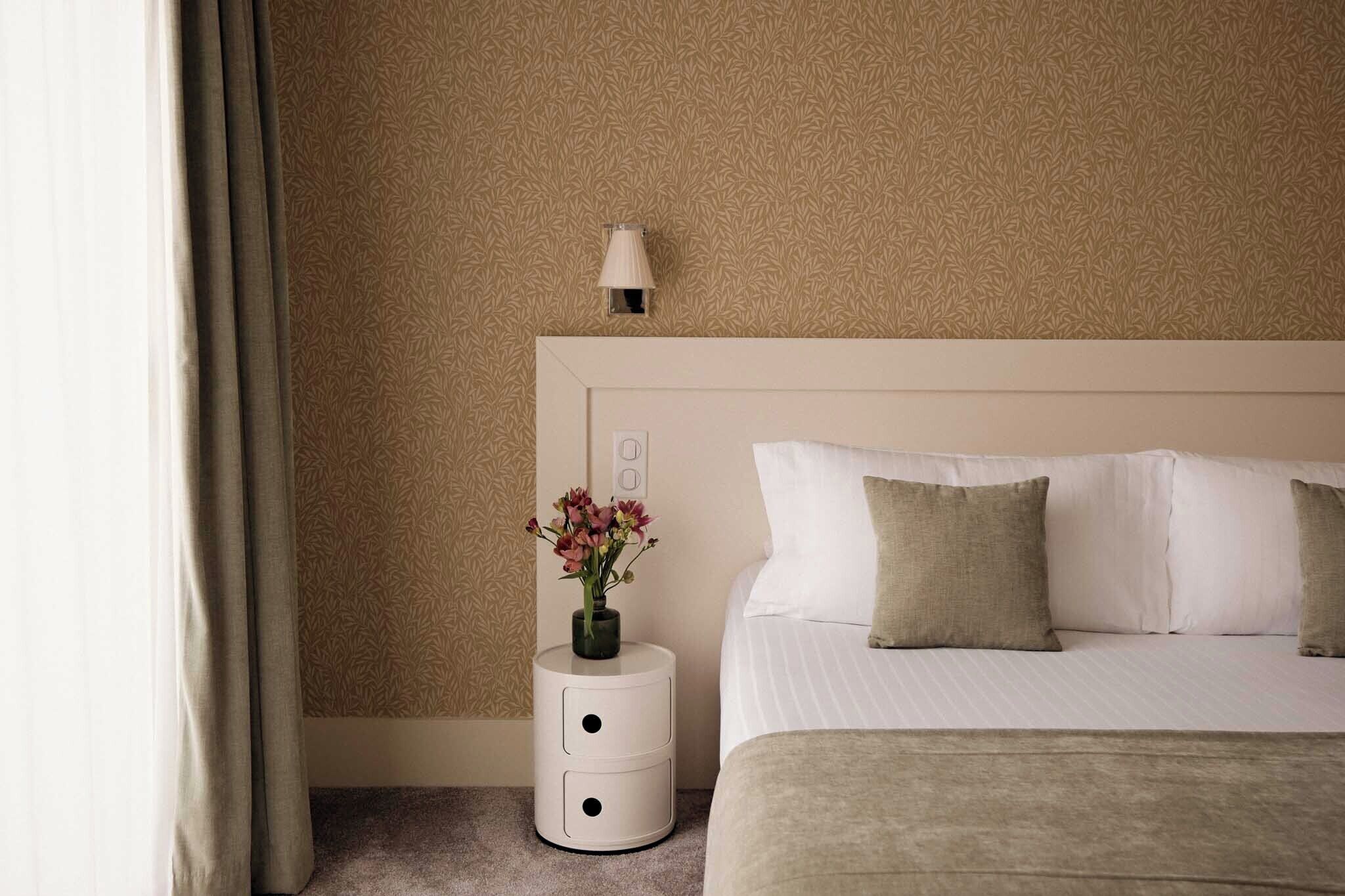A hotel room with a bed, a nightstand, a lamp, and a wall with a leaf pattern.