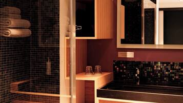 A modern bathroom with a glass shower enclosure, wooden cabinetry, and a black tiled backsplash.