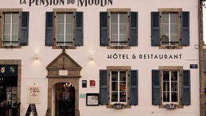 Een gebouw met de tekst 'La Pension du Moulin', waarop staat dat het een hotel en restaurant is. Er staan buiten tafels en stoelen.