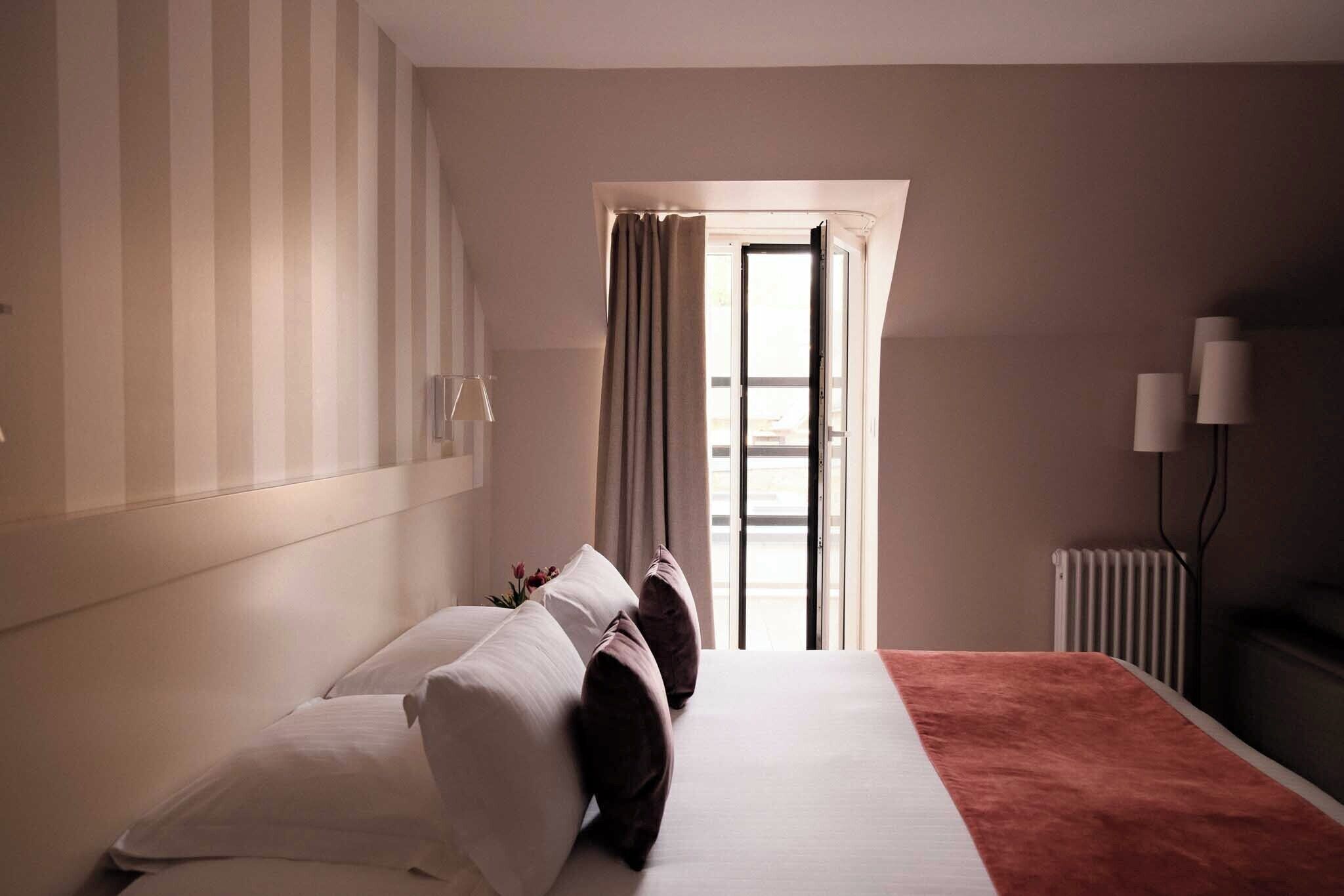 A hotel room with a bed, a radiator, a window with curtains, and a lamp.