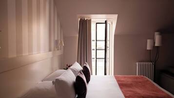 A hotel room with a bed, a radiator, a window with curtains, and a lamp.