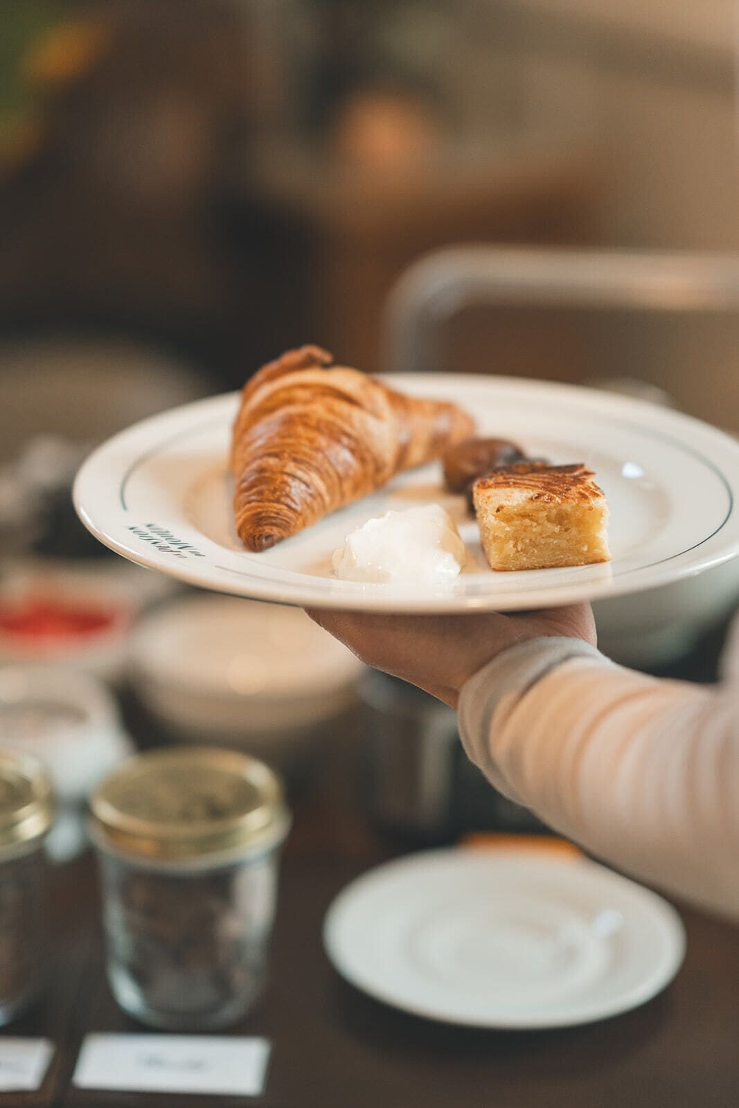 A person holding a plate with a croissant and a piece of bread.