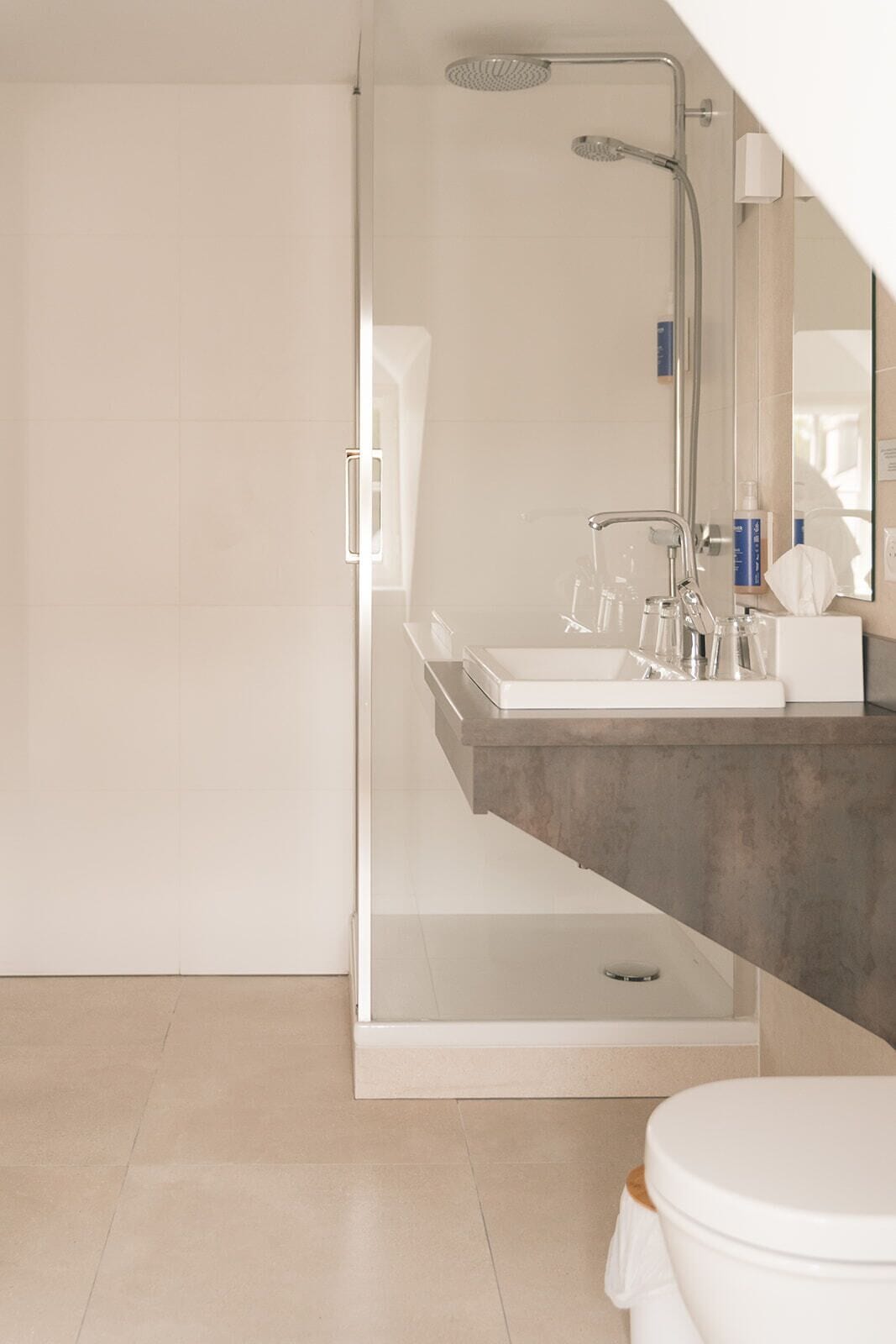 Une salle de bain moderne avec une douche à parois de verre, un grand miroir et un lavabo blanc doté d’un plan de travail.