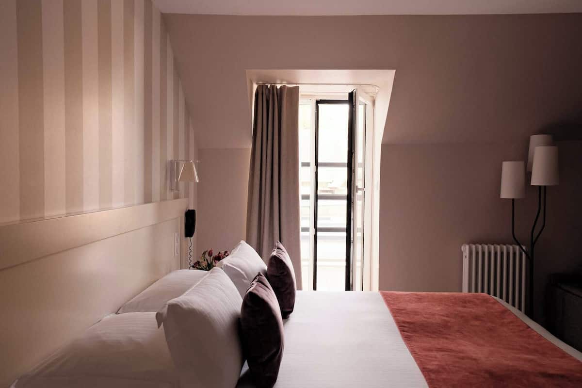 Een hotelkamer met een bed, een radiator, een lamp en een raam met gordijnen.