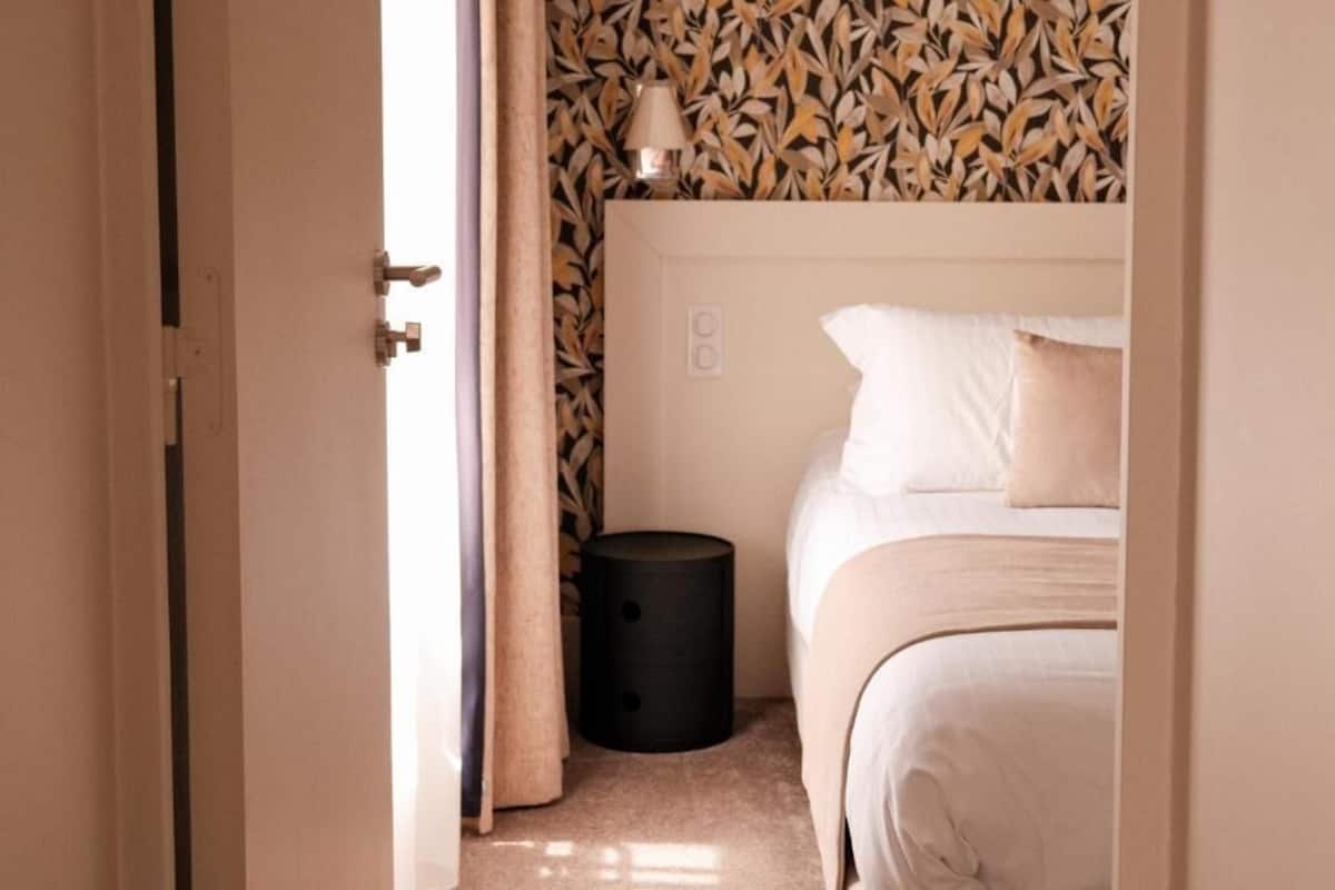 Een slaapkamer met een bed, een nachtkastje, een lamp en een muur met een bladmotief.