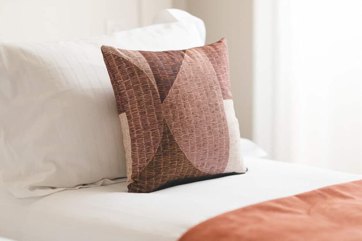 Een bed met een wit hoofdeinde, een gestreept kussen en een bruine deken.