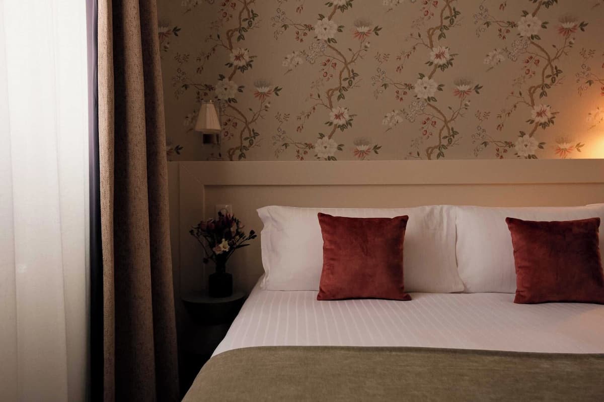 Een hotelkamer met een bed, een nachtkastje met een bloemenvaas en een behang met bloemenmotief.