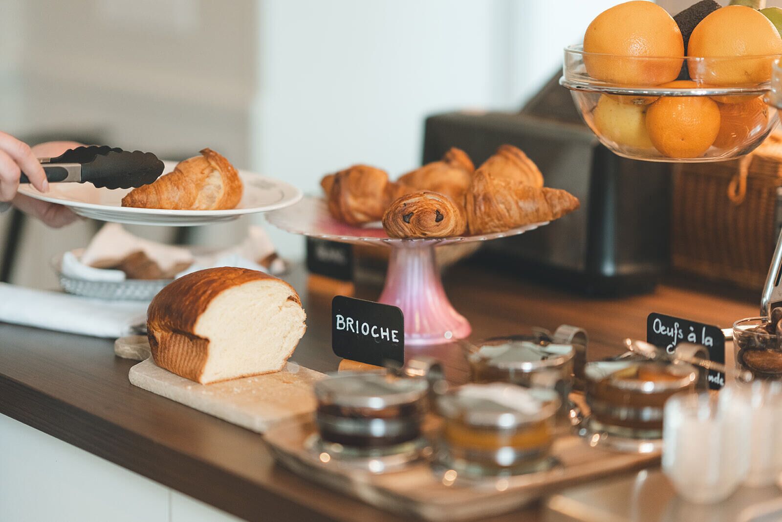 Una vitrina de panadería con croissants, pan y un bol de naranjas.