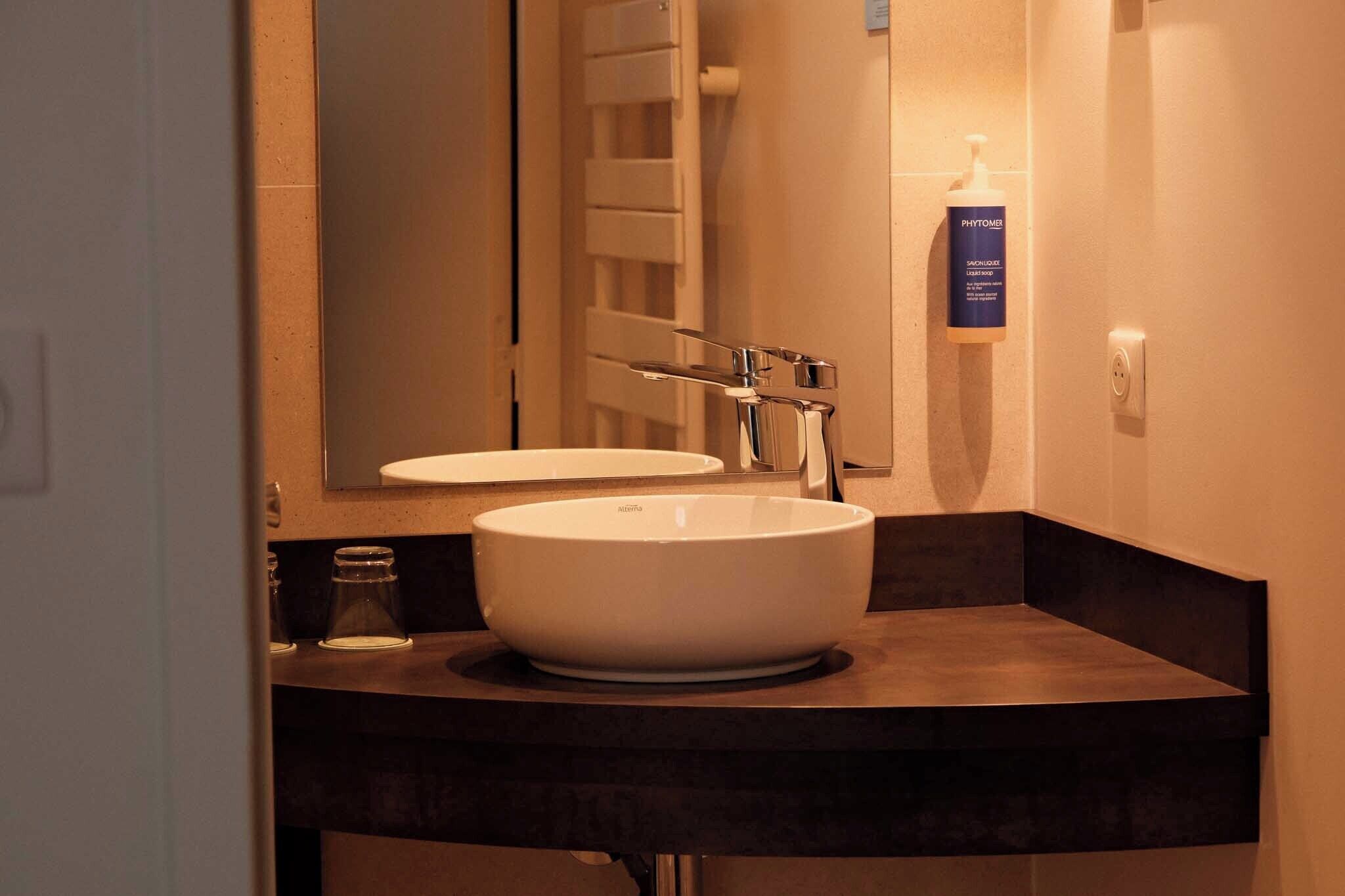 A bathroom with a white sink, a mirror, and a Phytomen brand bottle.