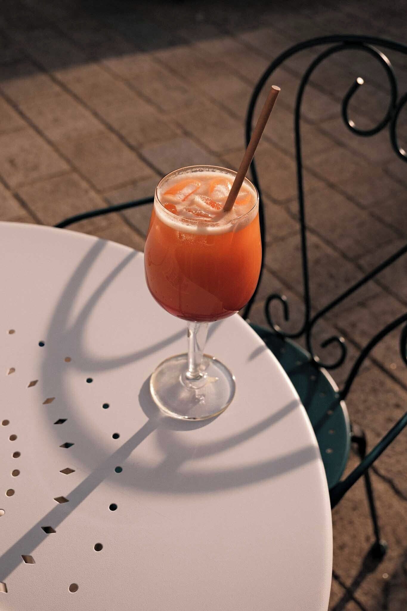 A glass of orange beverage on a white table with a metal chair in the background.