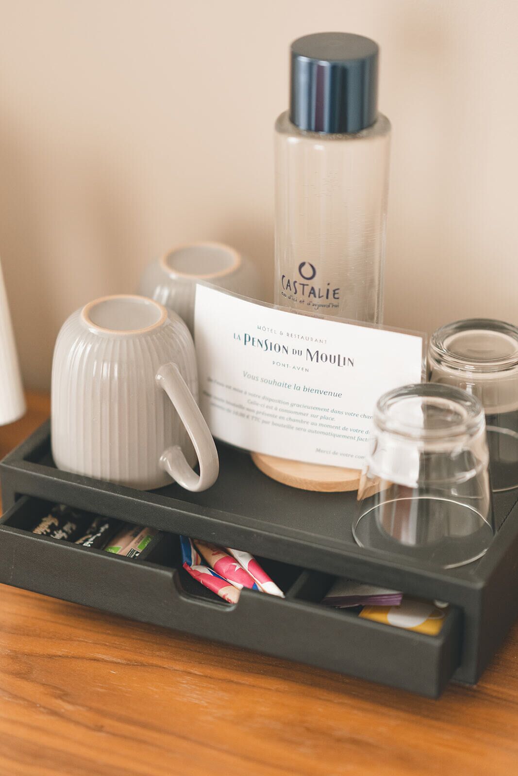 Une chambre d’hôtel avec un plateau contenant une théière, une bouteille, un verre et une carte de bienvenue.