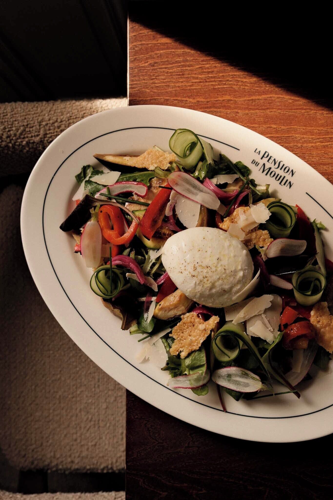 Une assiette remplie de différents légumes, accompagnée d’une cuillère de crème.