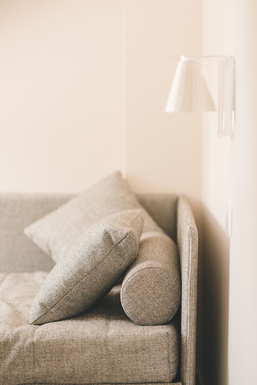 A sofa with a pillow and a lamp in a room with a plain wall.