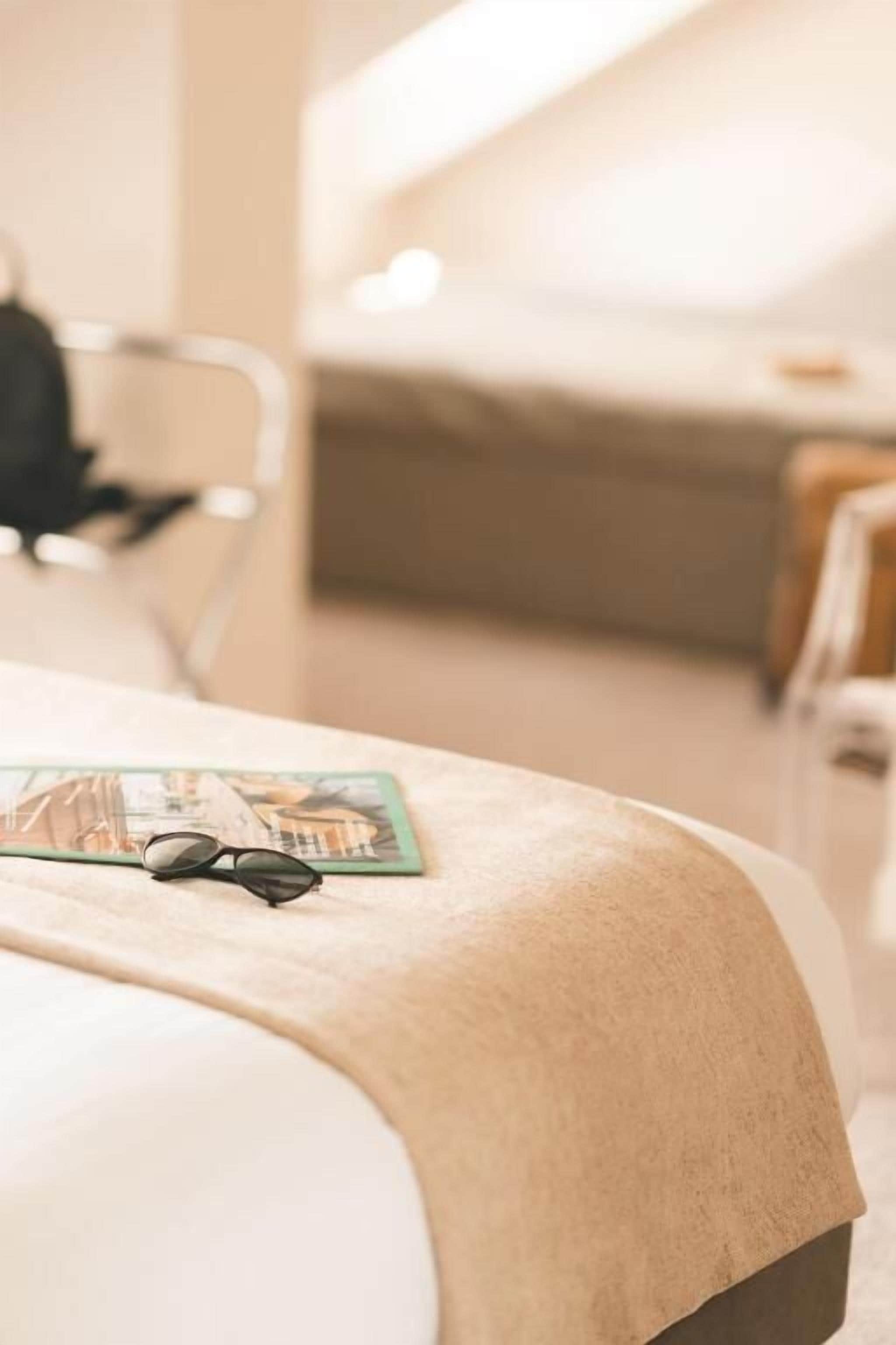 Una habitación de hotel con una cama, una revista y un par de gafas sobre la cama.