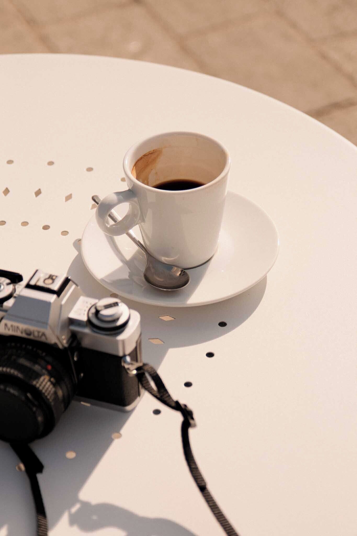 A white table with a cup of coffee and a camera.