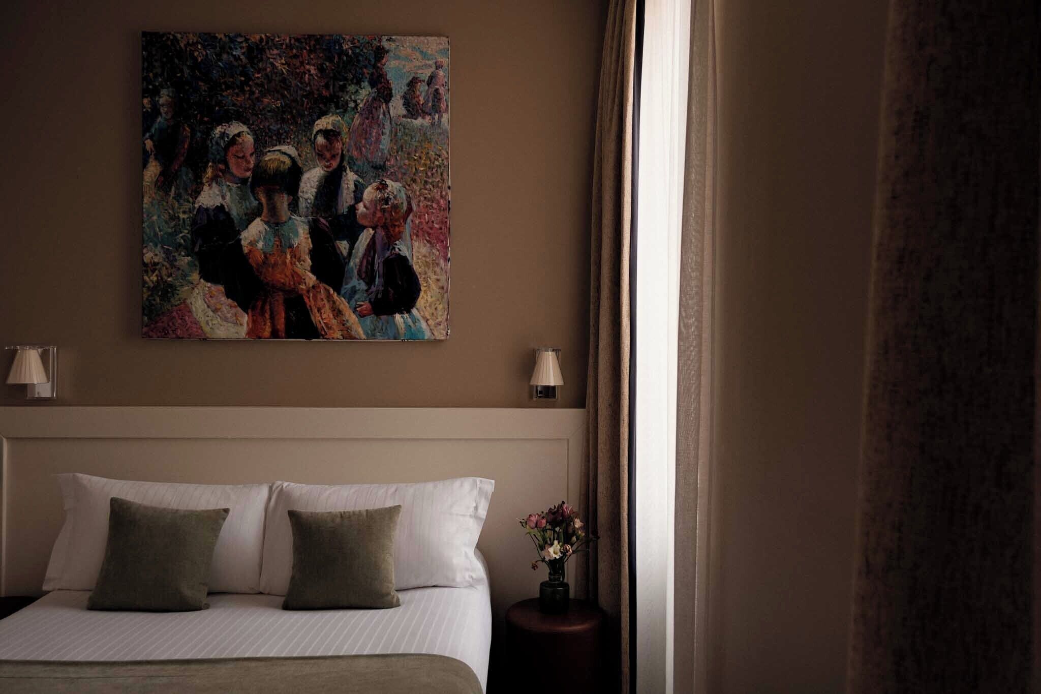 Una habitación de hotel con cama, almohadas, un cuadro en la pared, una mesita de noche y una lámpara.