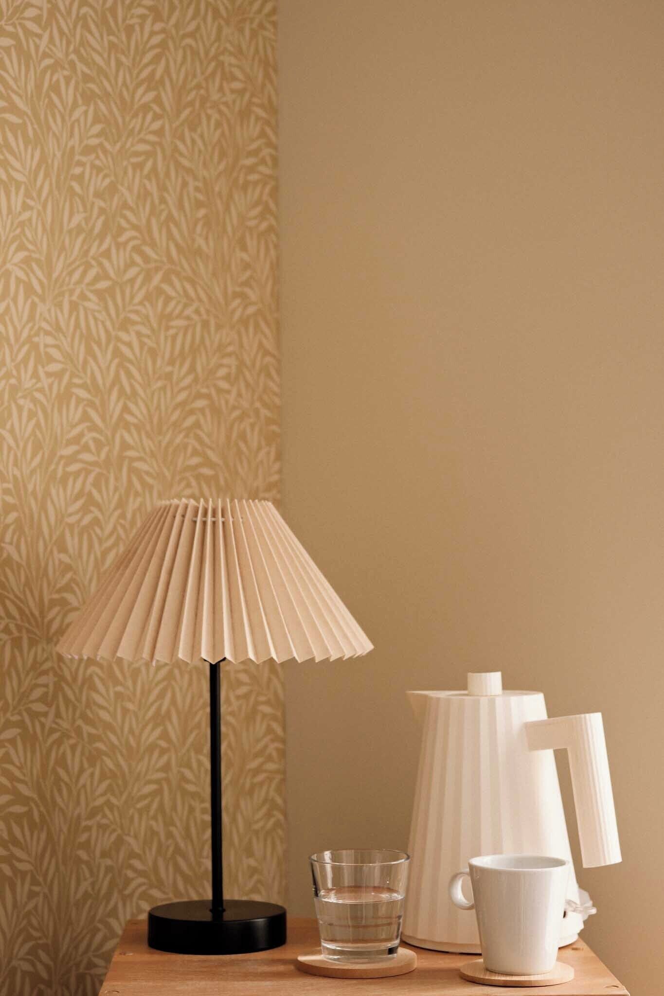 Une table avec une lampe, un verre, une tasse et un pichet blanc.