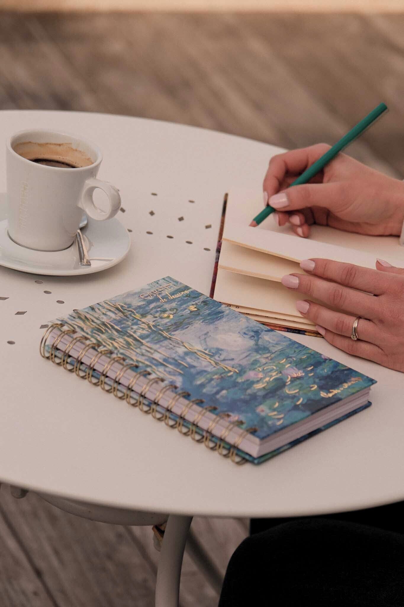 A table with a notebook, a cup of coffee, and a pen.