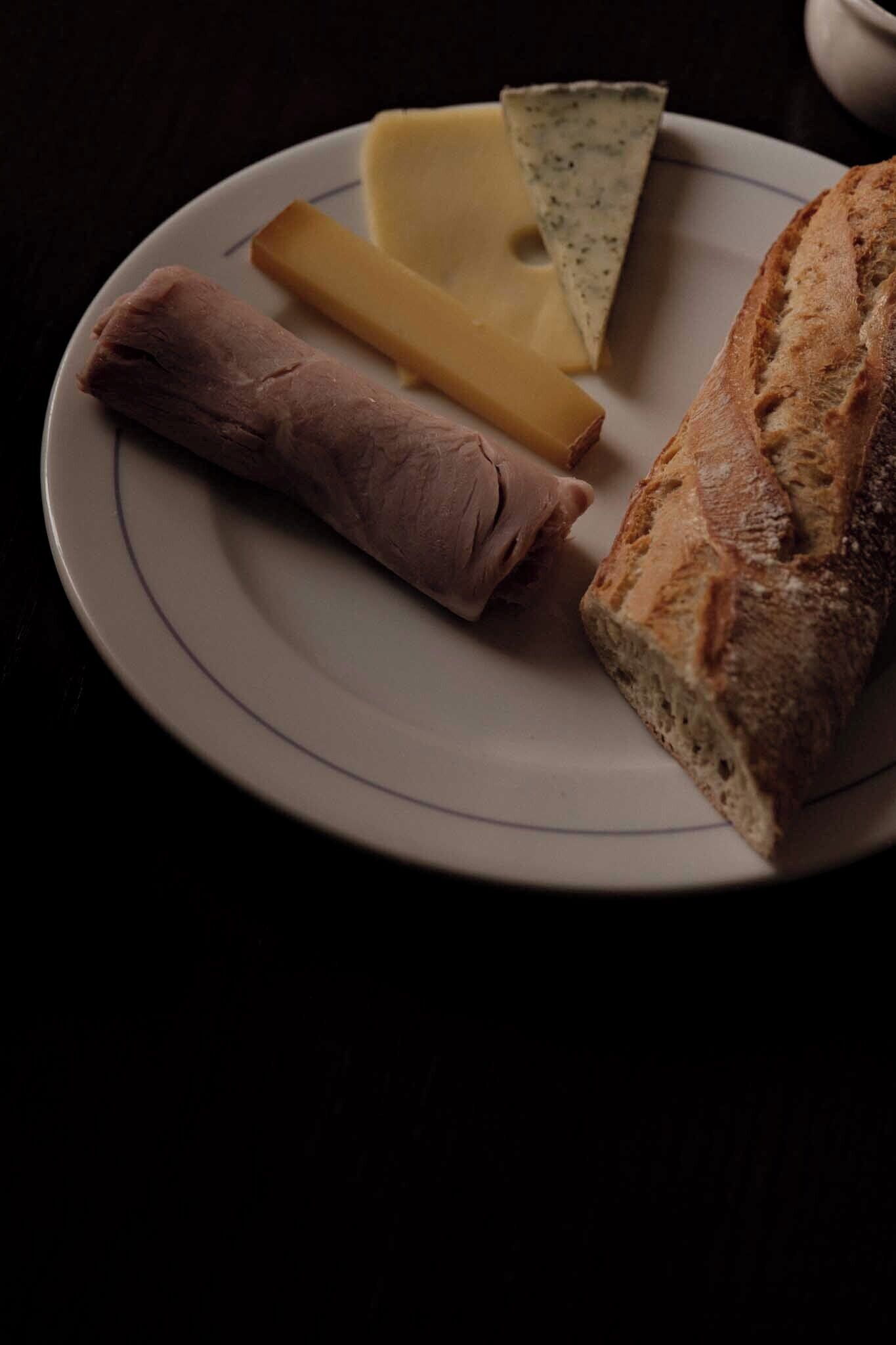En tallrik med en bit kött, en skiva ost, en bit ost och en limpa bröd.
