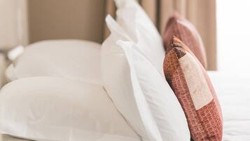 Un letto con cuscini bianchi e un singolo cuscino marrone, una tenda color beige e una lampada bianca in una camera d'albergo.