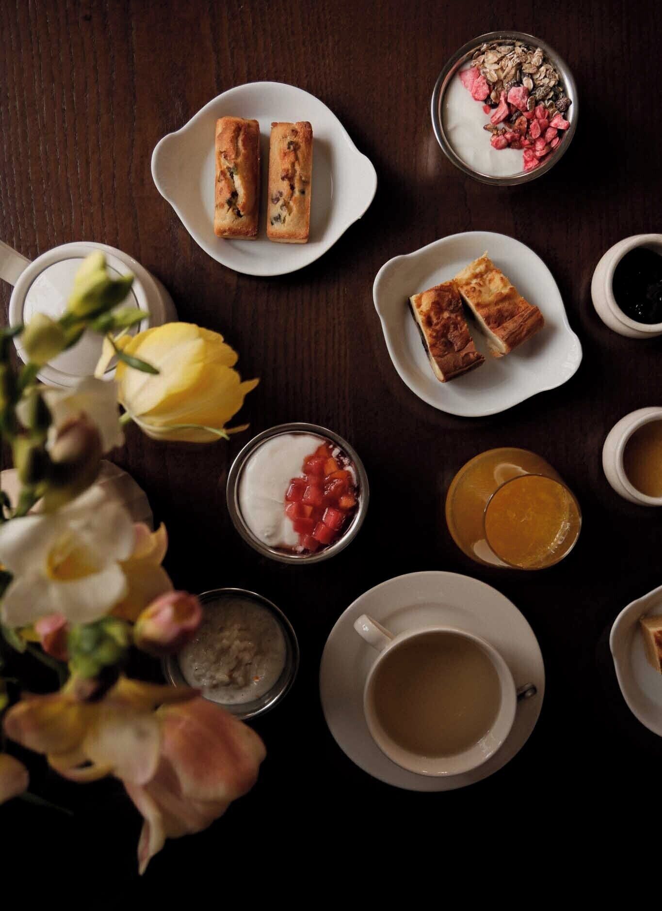 A table with various food items, including pastries, yogurt with fruit, and a cup of tea.